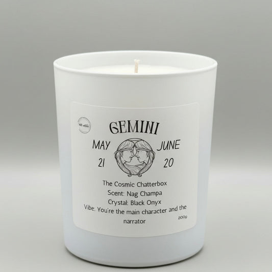 White candle with a label detailing the Gemini zodiac sign on a gray background