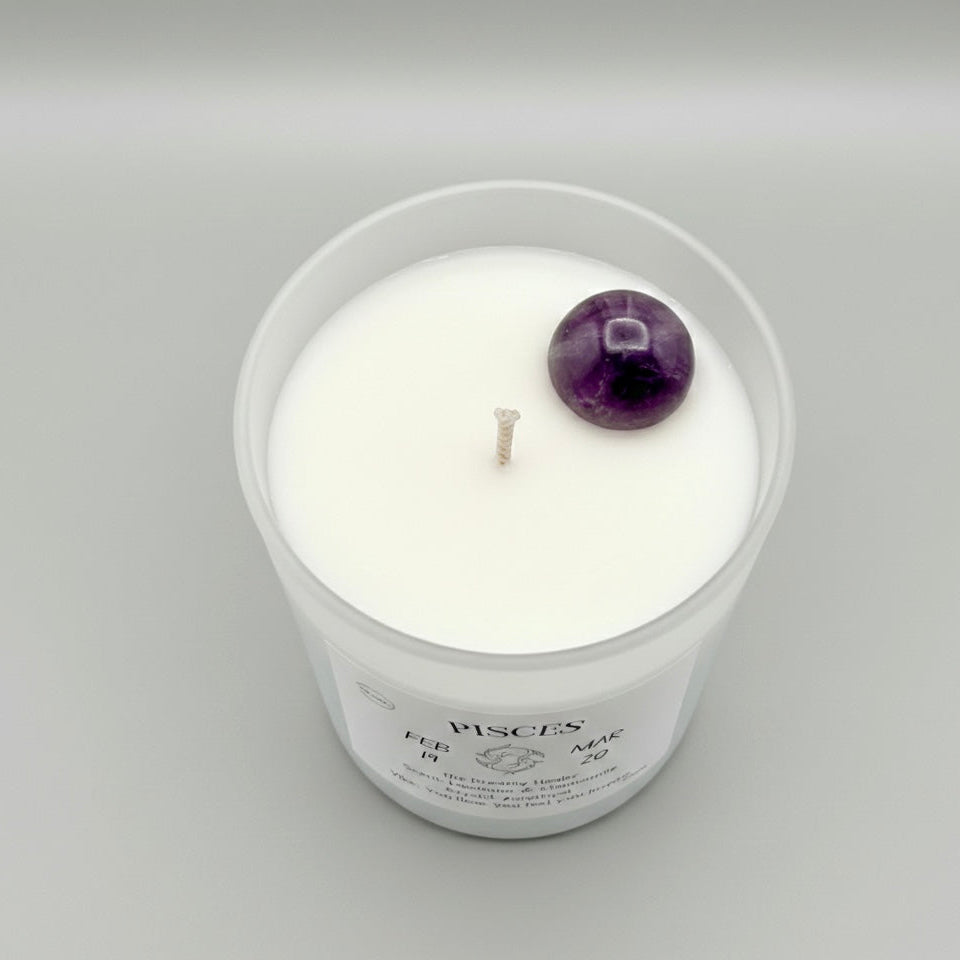 White candle in a glass jar with an amethyst gemstone on a gray background