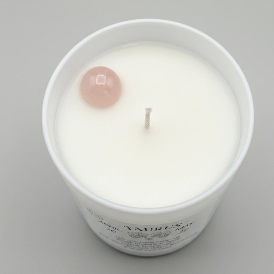 White candle in a glass jar with a pink crystal on top against a gray background