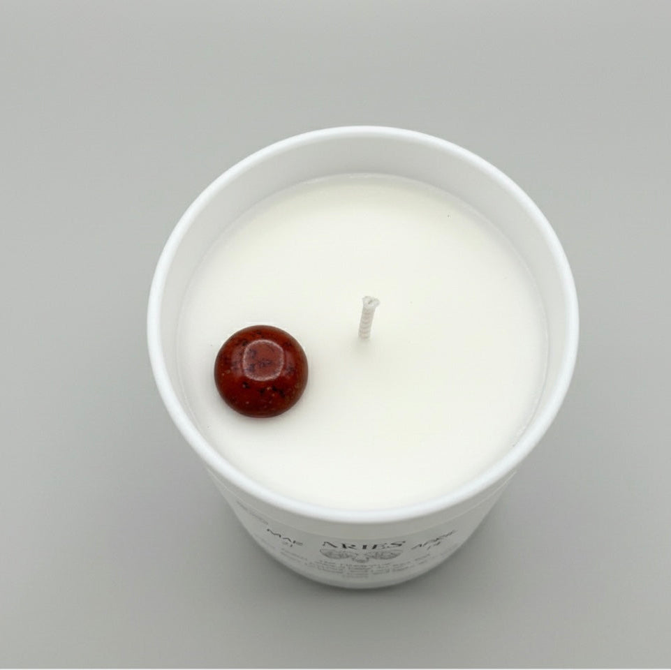 White candle in a glass jar with a red wick on a gray background