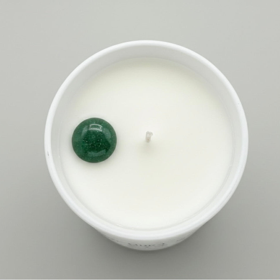 White candle with a green gemstone on a gray background