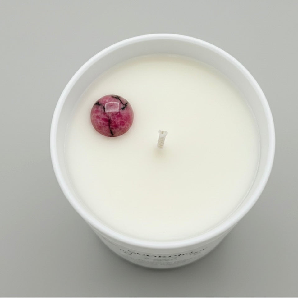 White candle in a container with a pink and black decorative element on a gray background