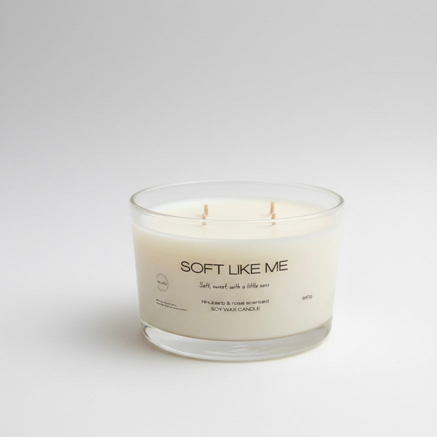 Candle in a glass jar labeled 'Soft Like Me' on a white background