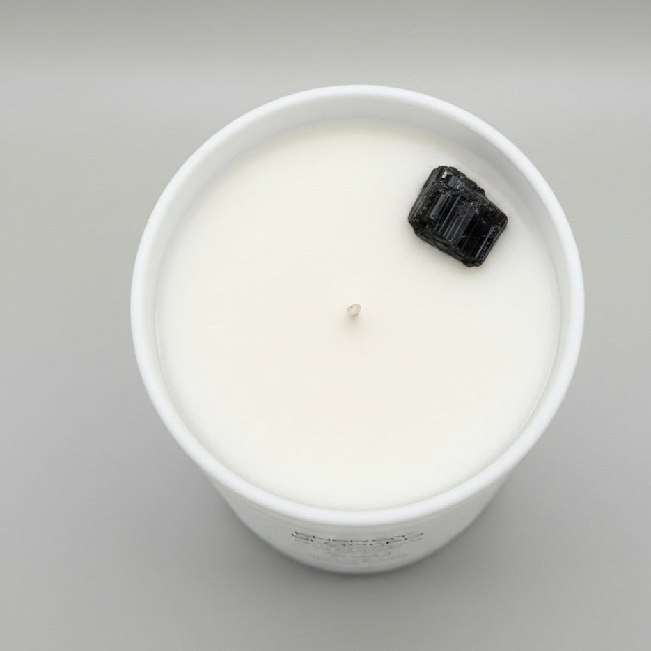 White candle in a glass jar with a black decorative element on a gray background