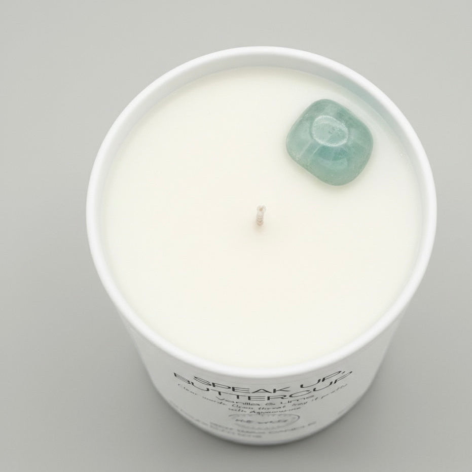 White candle in a container with a green gemstone on a gray background