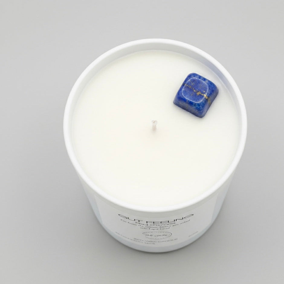 White candle in a glass jar with a blue decorative stone on a gray background
