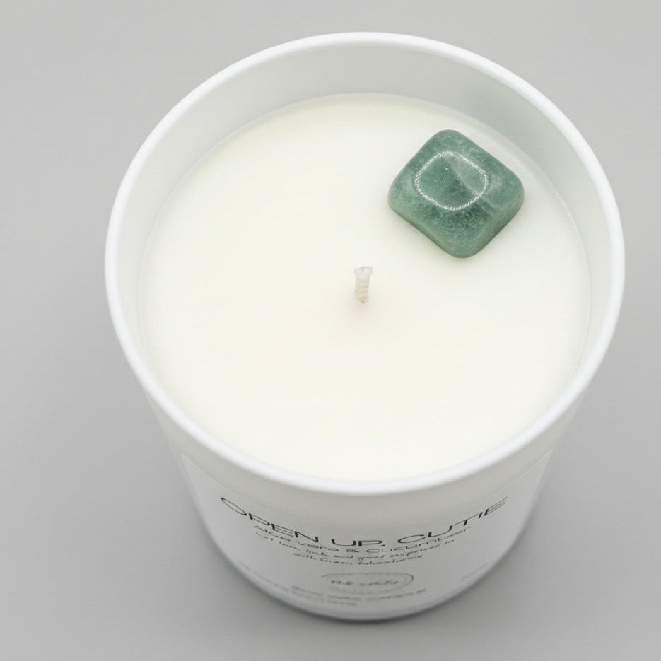 White candle in a glass jar with a green stone on a gray background